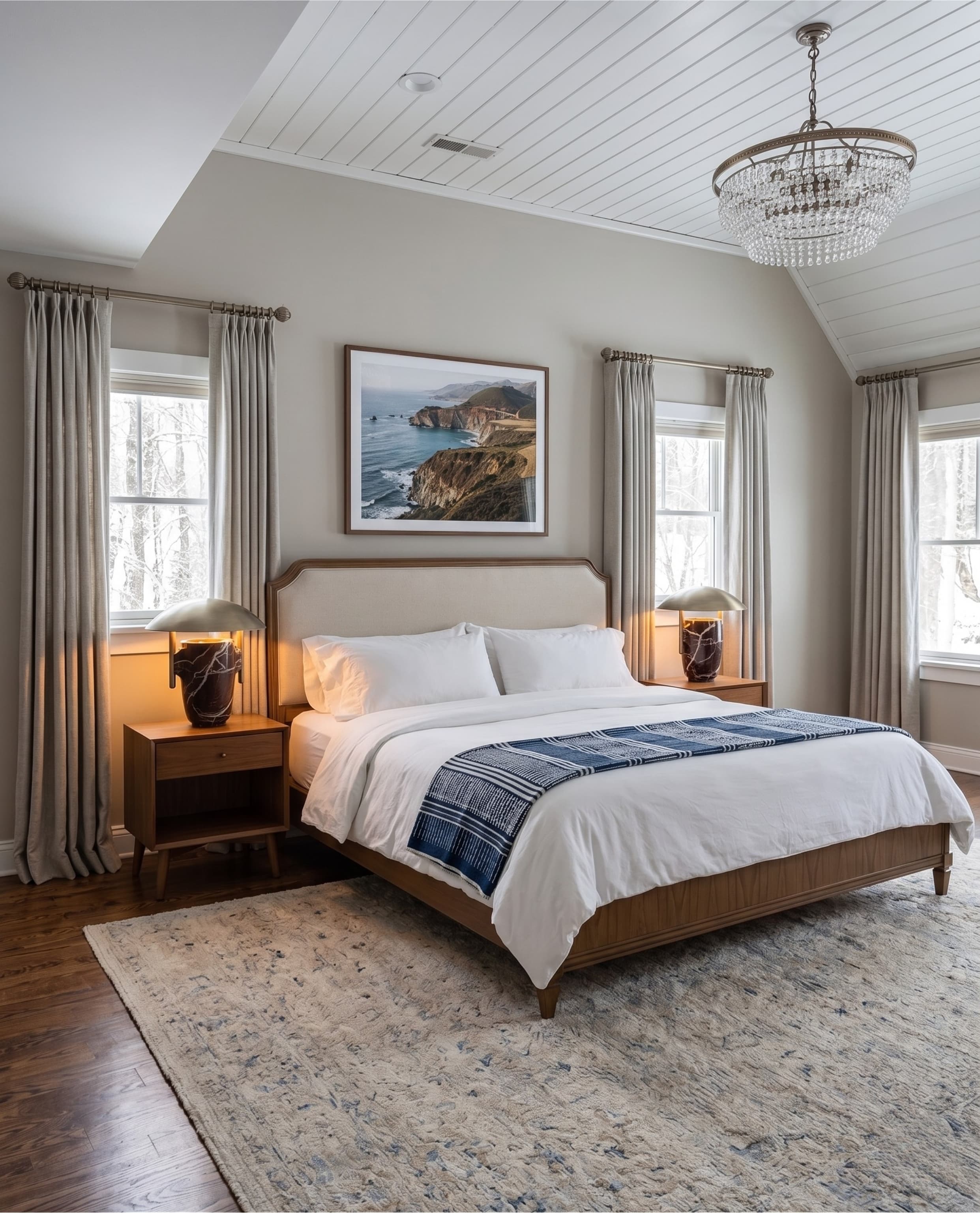 Modern bedroom with white bedding, blue throw, coastal wall art, and a sparkling crystal chandelier.